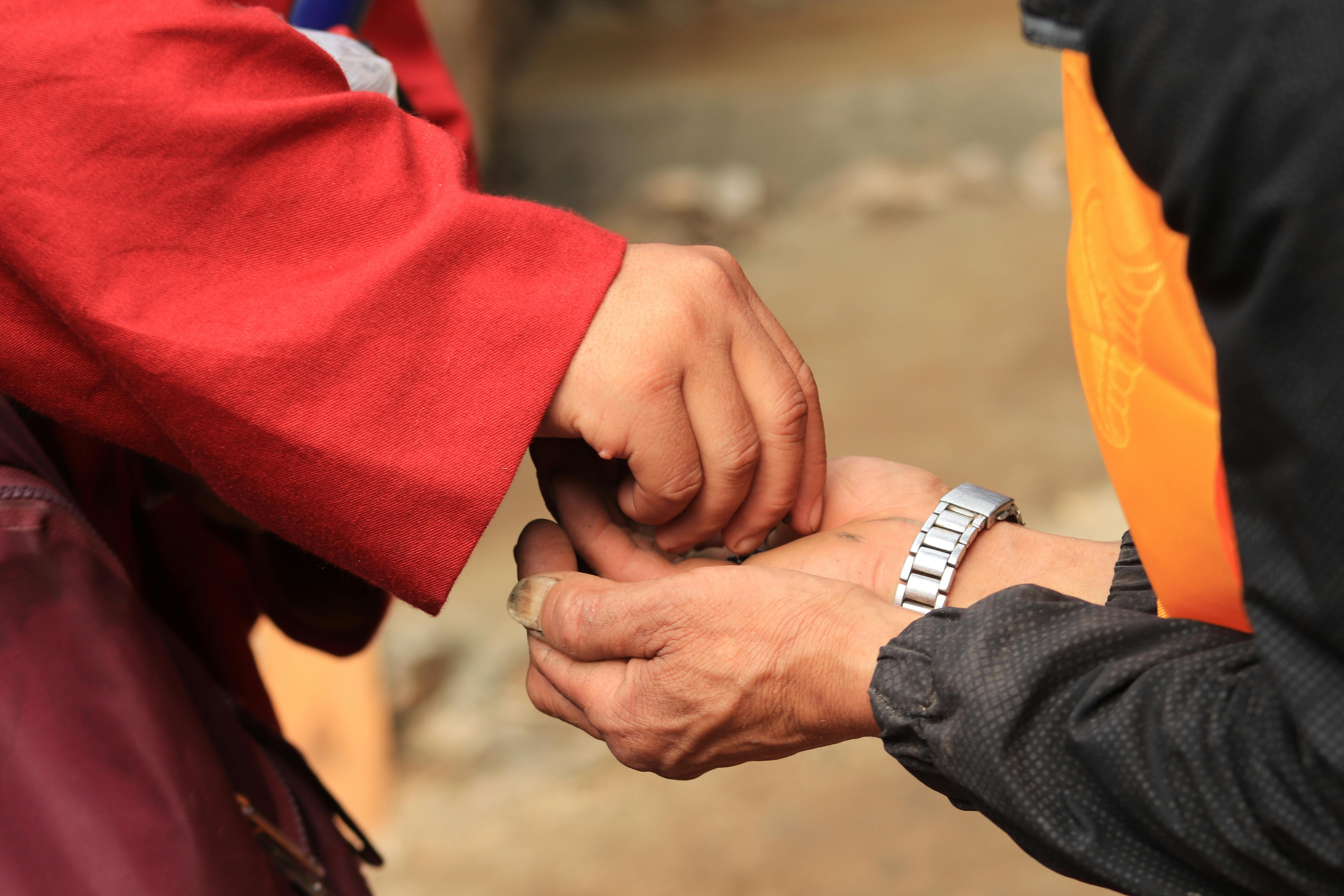 Close-up of two people exchanging small items with hands against a blurred outdoor background.