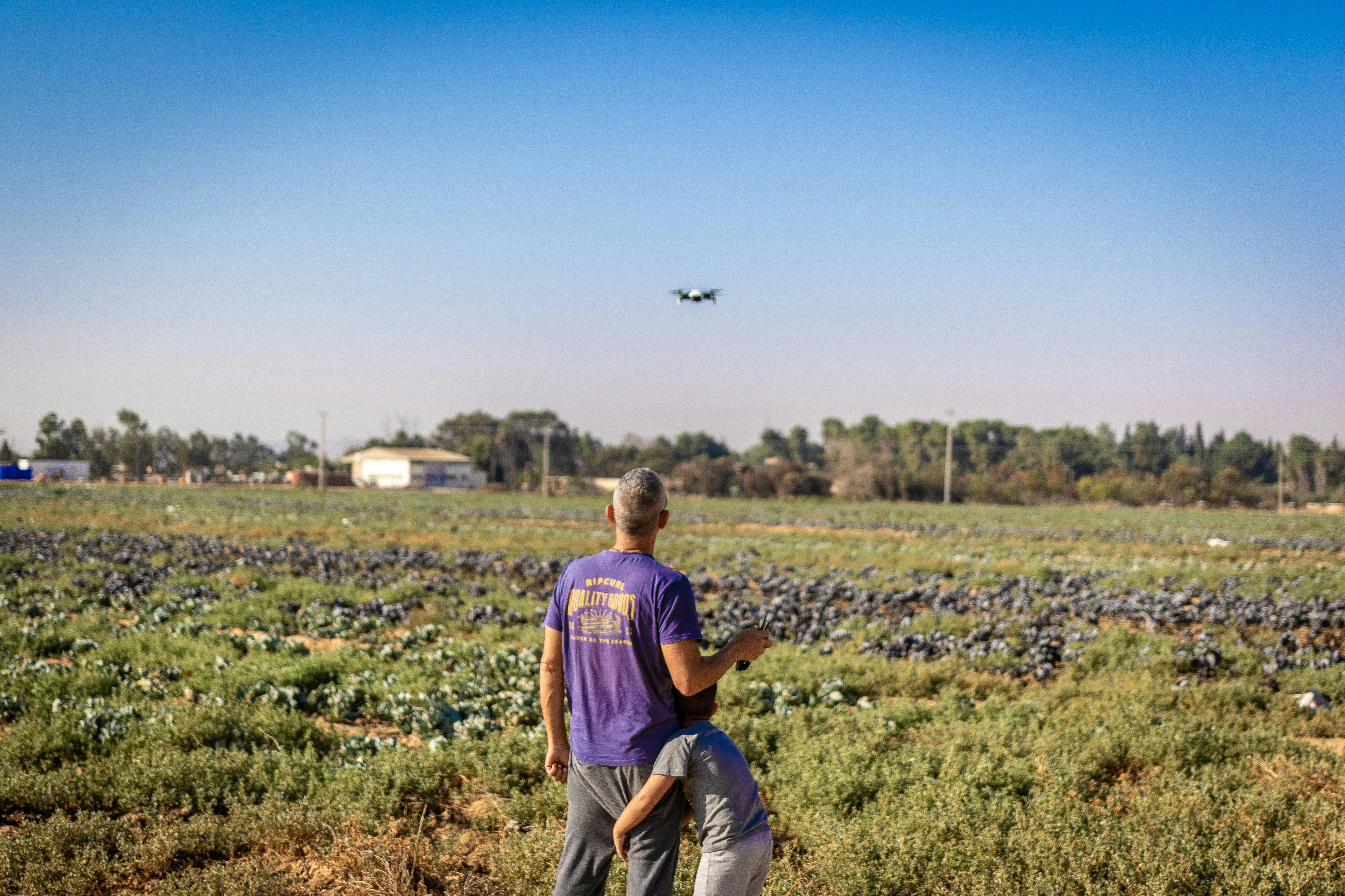 Blog Man and child fly drone over green farmland, capturing scenic rural landscape.